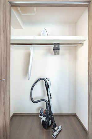 A compact room with a vacuum cleaner, a white shelf, and a hanging towel. - Dash Living Osaki (Shinagawa-ku)