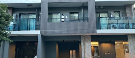 A multi-story building with a modern architectural design, featuring balconies, large windows, and a gated entrance.