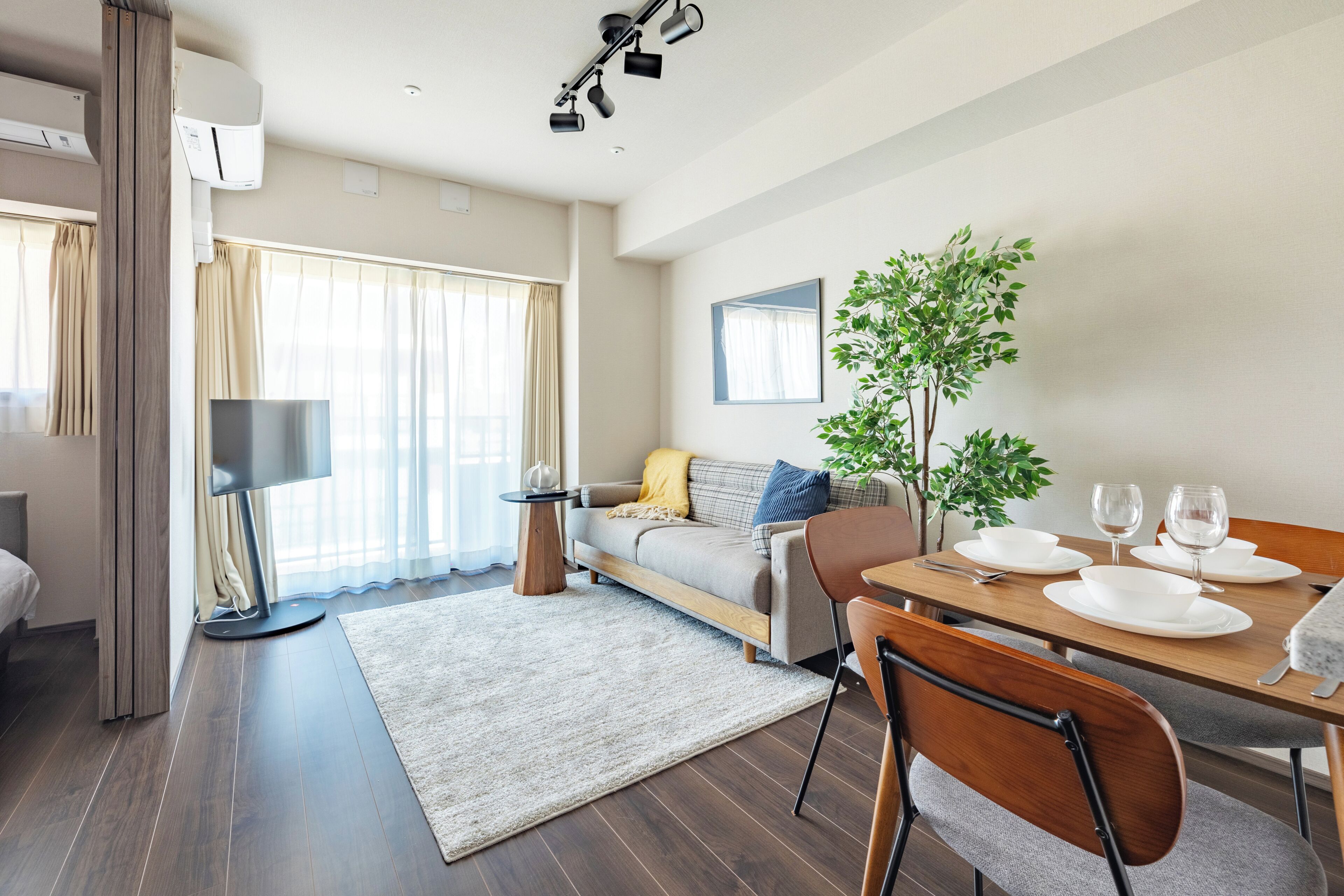 A modern living room with a sofa, dining table, and a potted plant.