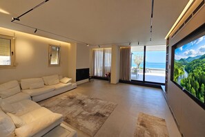 A modern living room with a sectional sofa, a flat-screen TV, and a large window with a scenic view. - La Terrazza Azzurra, Vlore, Albania (Vlore)