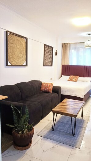 A room with a sofa, a bed, a coffee table, a potted plant, and artwork on the walls. - Prime Kilimani Location,5 mins Walk to Yaya Centre, Mersen Studio (Nairobi)