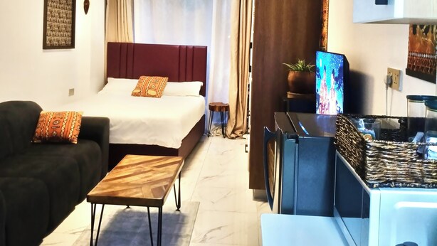 Habitació d'hotel amb llit, sofà, taula petita, zona de cuina amb cafetera i televisió.