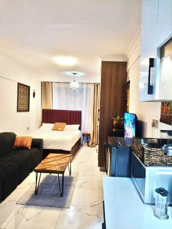 A hotel room with a bed, a sofa, a small table, a kitchen area with a coffee machine, and a television. - Prime Kilimani Location,5 mins Walk to Yaya Centre, Mersen Studio (Nairobi)