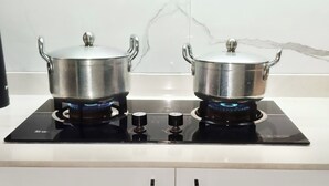 Una cuina amb dues olles d'acer inoxidable sobre una fogaira d'inducció negra, armaris blancs a la part inferior i un relleu de marbre.