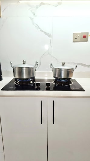 A kitchen with two stainless steel pots on a black induction cooktop, white cabinets below, and a marble backsplash. - Prime Kilimani Location,5 mins Walk to Yaya Centre, Mersen Studio (Nairobi)