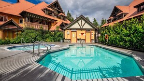 Un espace piscine comprenant deux piscines, une terrasse en bois et un bâtiment doté d’un toit triangulaire.