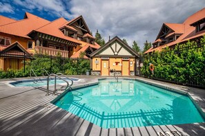 Ein Poolbereich mit zwei Pools, einer Holzterrasse und einem Gebäude mit einem Dreiecksdach.