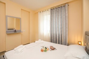 A hotel room with a bed, a mirror, a window with curtains, a bedside table with a lamp, and a magazine. - Velaris Partial Sea View Balcony 101, Vlore, Albania (Vlore)