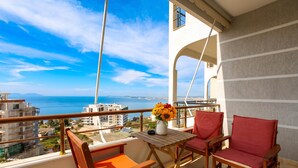 A balcony with a view of the sea, a table with a vase of flowers, and two red chairs. - Vlora Sunset Apartment /w Balcony & Sea View, Vlore, Albania (Vlore)