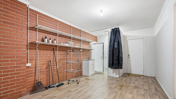 A room with a brick wall, white shelves, a white door, and a shower area. - Stylish West Hobart Villa (West Hobart)