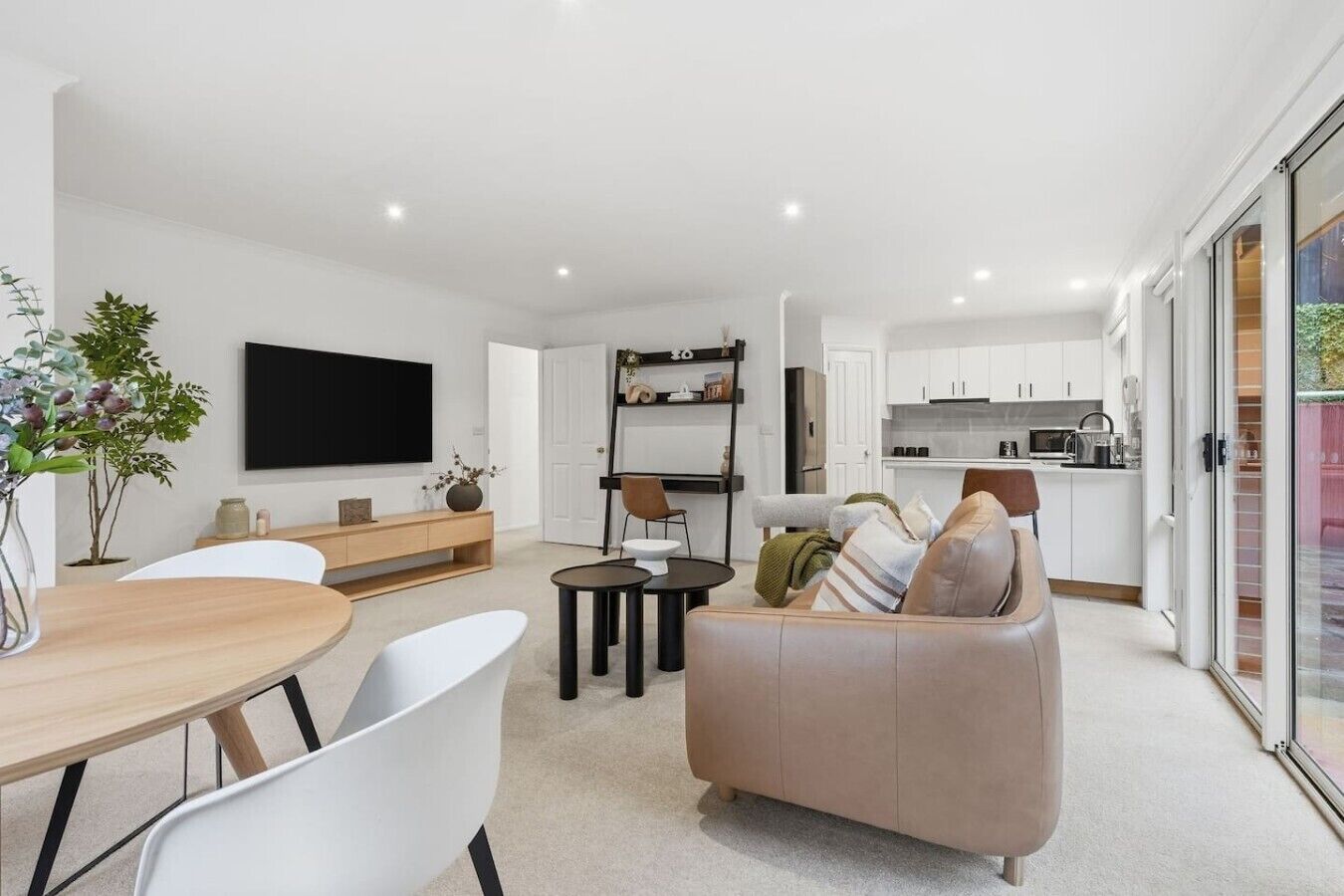 A modern living room with a sofa, a dining table, and chairs. There is a kitchen area with cabinets and appliances.