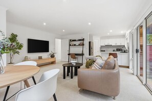 Una sala de estar moderna con un sofá, una mesa de comedor y sillas. Se observa una zona de cocina con armarios y electrodomésticos.