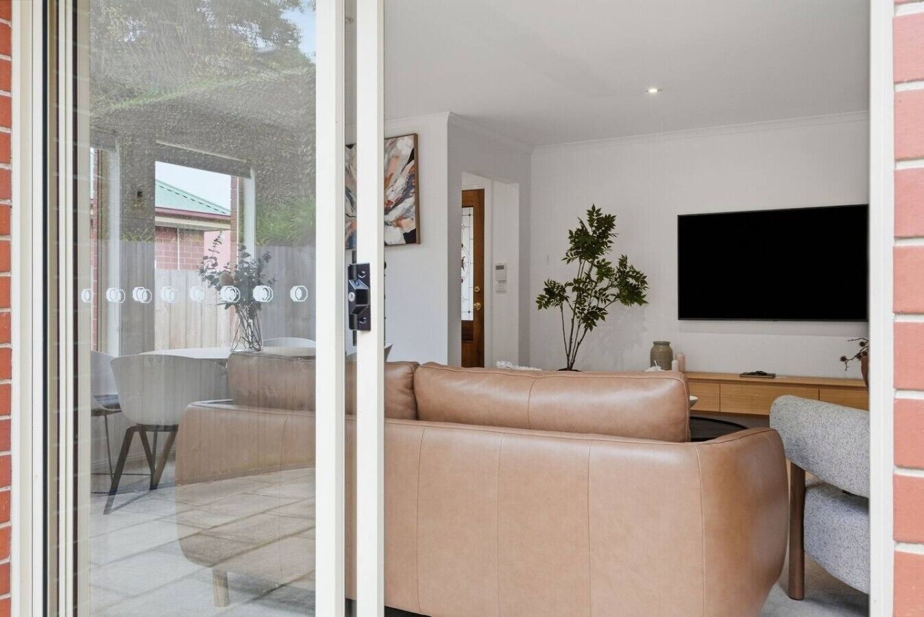 A modern living room with a leather sofa, a flat-screen TV, and a dining area with chairs and a table.