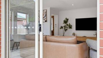 A modern living room with a leather sofa, a flat-screen TV, and a dining area with chairs and a table.