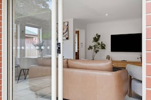 A modern living room with a leather sofa, a flat-screen TV, and a dining area with chairs and a table. - Stylish West Hobart Villa (West Hobart)
