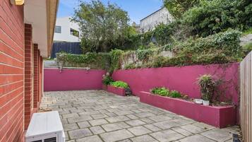 A paved patio area with a red wall and planters, a white air conditioning unit, and a brick wall.