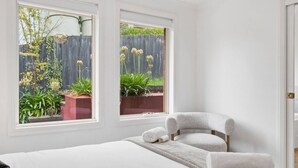 A bedroom with a bed, a chair, and two windows overlooking a garden. - Stylish West Hobart Villa (West Hobart)