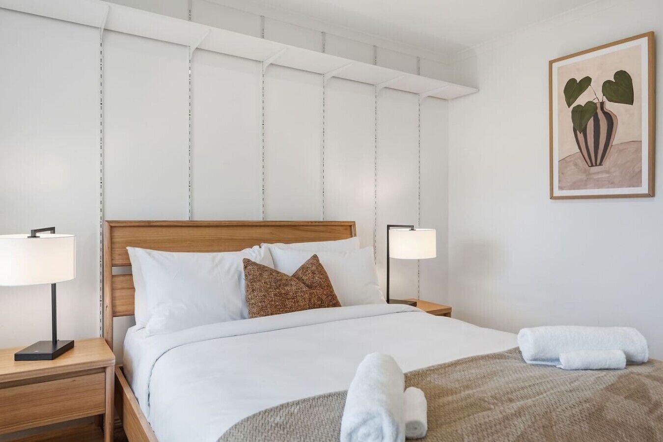 A neatly made bed with white linens and a brown pillow, flanked by two bedside lamps on wooden nightstands.