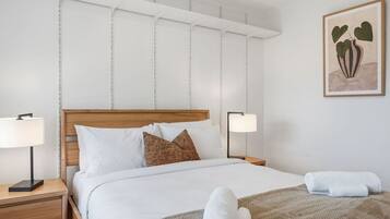 A neatly made bed with white linens and a brown pillow, flanked by two bedside lamps on wooden nightstands.