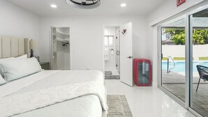 Ein modernes Hotelzimmer mit einem großen Bett, einem begehbaren Kleiderschrank, einer Glastür zu einem Poolbereich und einem roten Schrank.