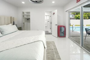 Ein modernes Hotelzimmer mit einem großen Bett, einem begehbaren Kleiderschrank, einer Glastür zu einem Poolbereich und einem roten Schrank.