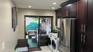 A compact kitchen with a stainless steel refrigerator, a washing machine, and dark wooden cabinets.