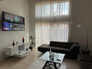 Ein Wohnzimmer mit Flachbildfernseher, einer Couch, einem Glastisch und einer Zimmerpflanze.