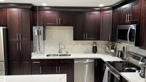 A modern kitchen with dark wood cabinets, stainless steel appliances, a marble countertop, and a built-in dishwasher.