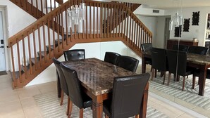 A dining area with a wooden staircase, a marble table, and black chairs.