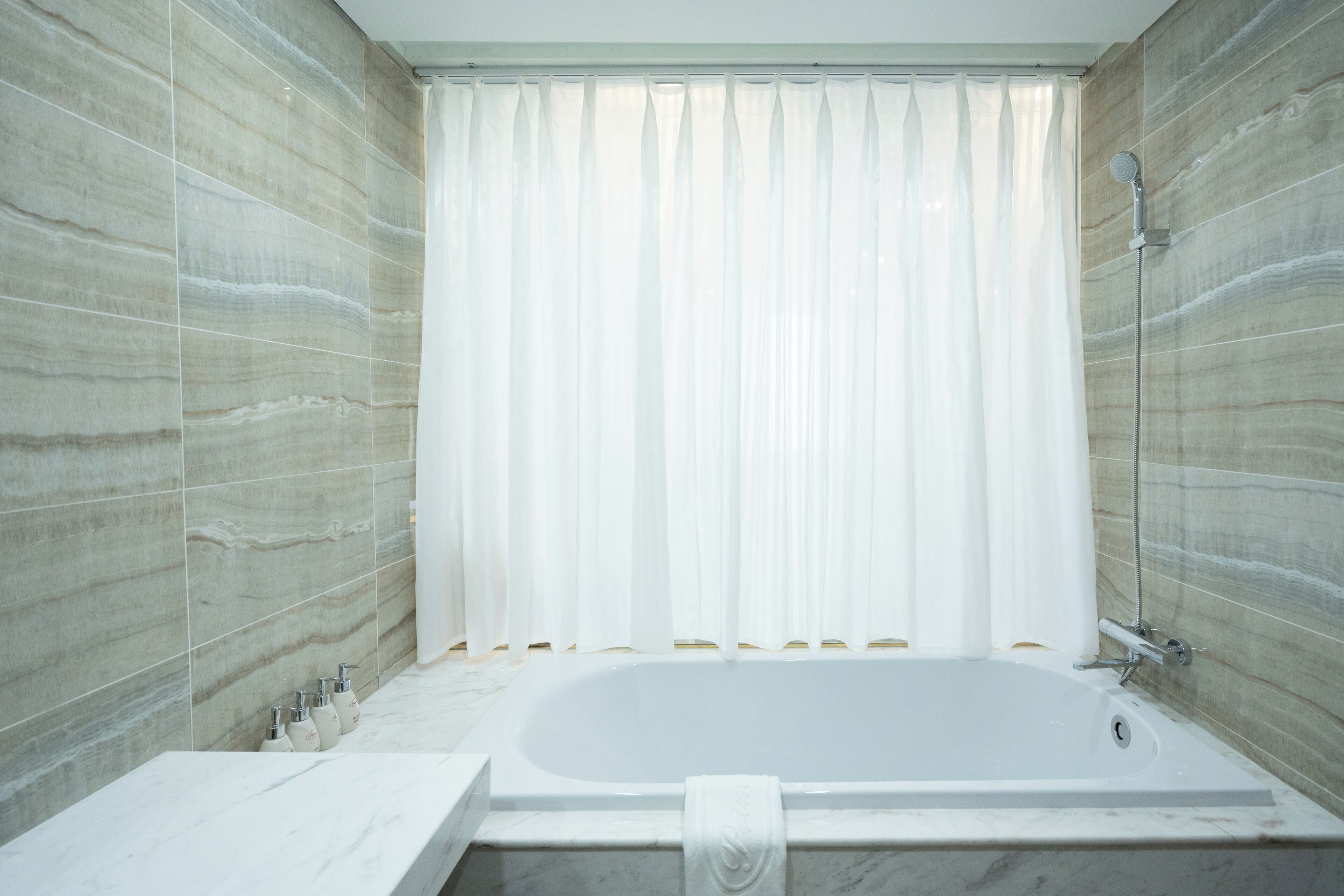 A modern bathroom with a large bathtub, marble walls, and a shower area.