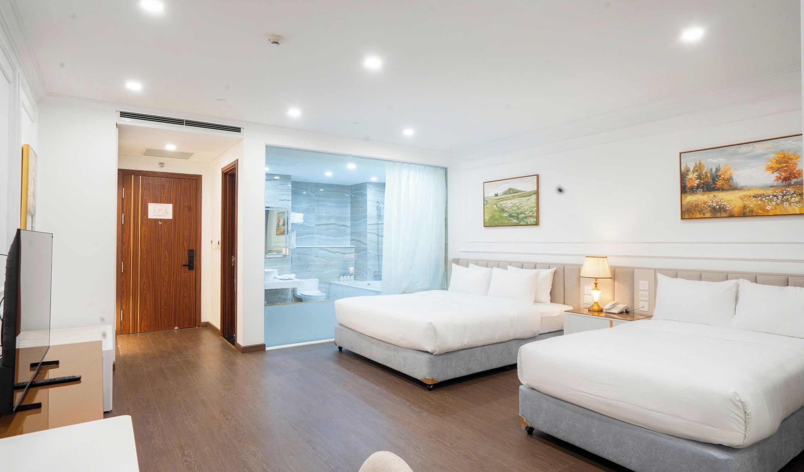 A hotel room with two beds, a bathroom, a desk, and a painting on the wall.