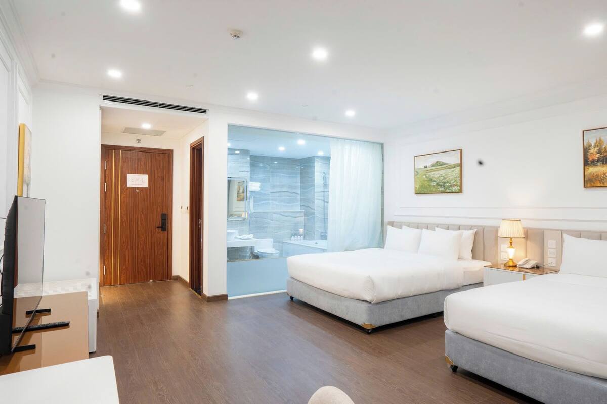 A hotel room with two beds, a bathroom, a desk, and a painting on the wall.