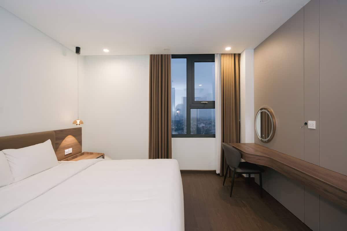 A hotel room with a bed, a desk, a chair, a window with curtains, and a view of the cityscape.