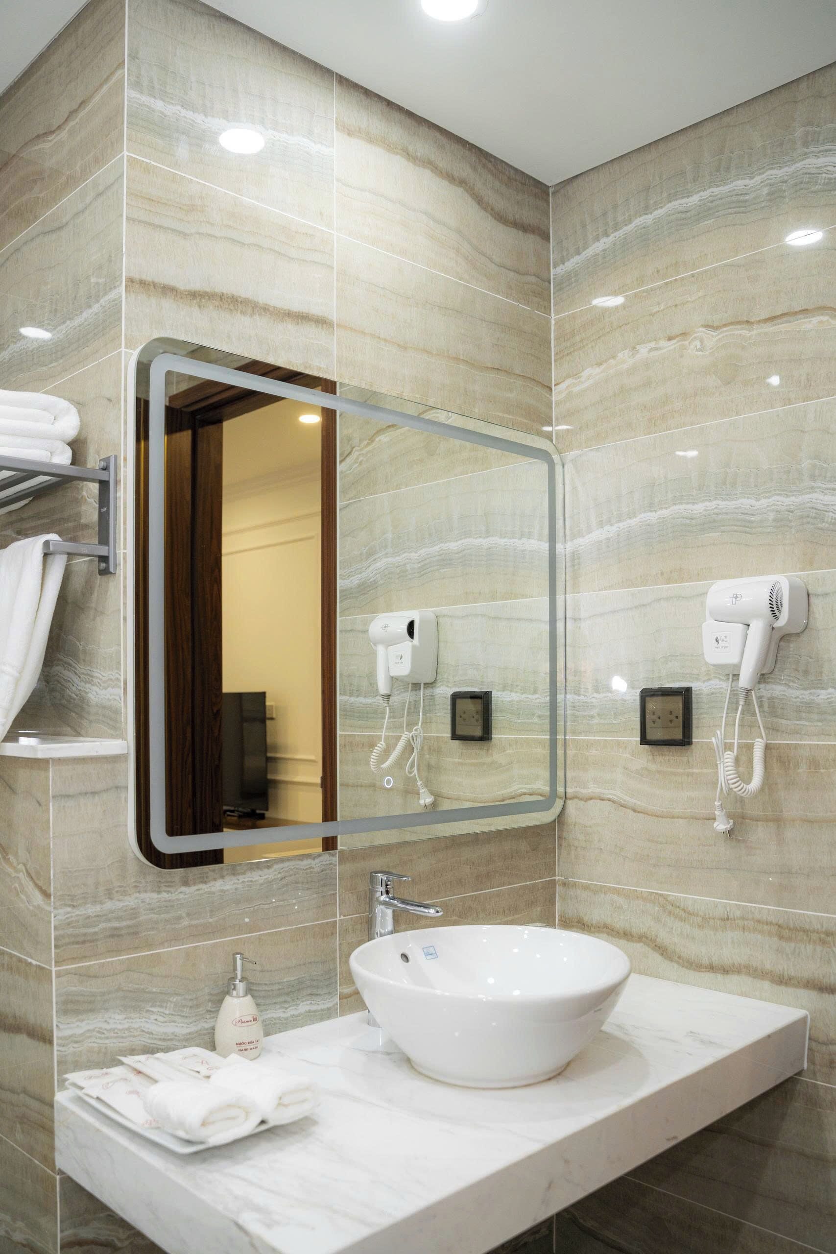 A bathroom with a marble wall, a large mirror, a sink, a hairdryer, and a towel rack.