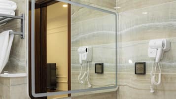 A bathroom with a marble wall, a large mirror, a sink, a hairdryer, and a towel rack.