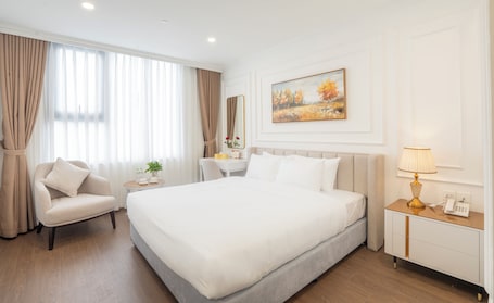 A hotel room with a large bed, a chair, a bedside table, a lamp, and a painting on the wall.. Prime Hotel Thai Nguyen