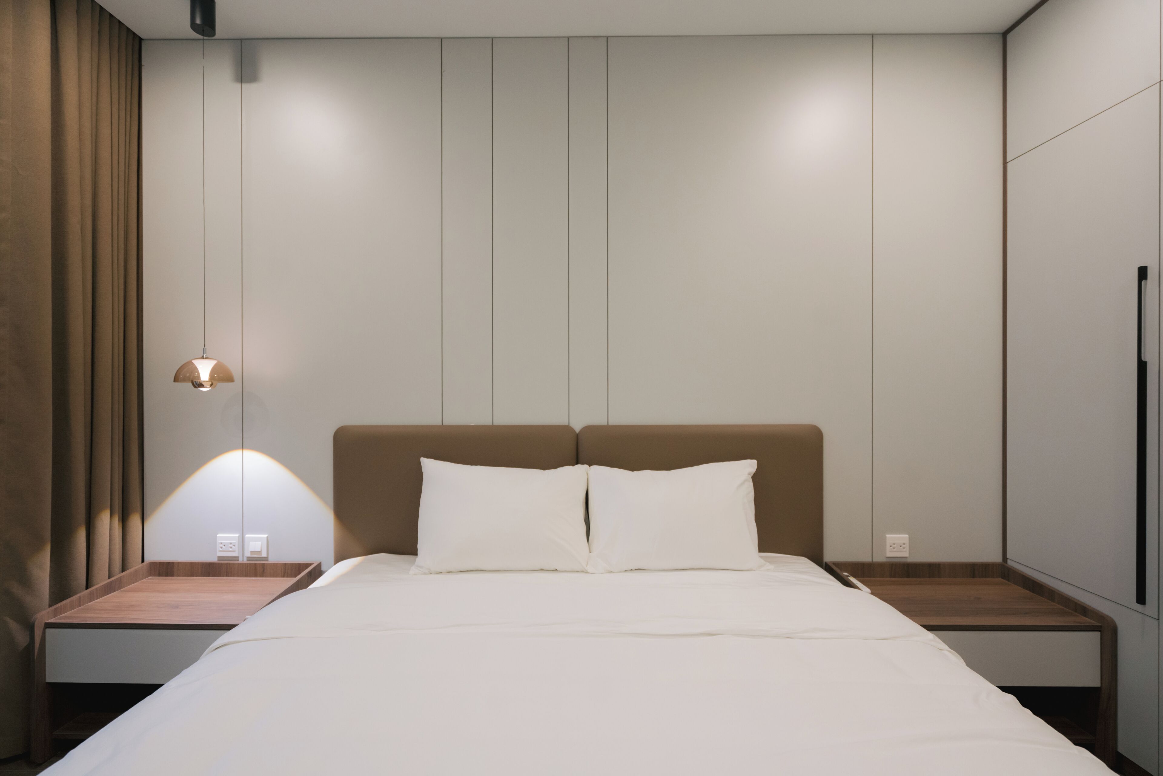 A modern hotel room with a bed, nightstands, a lamp, and a wardrobe.