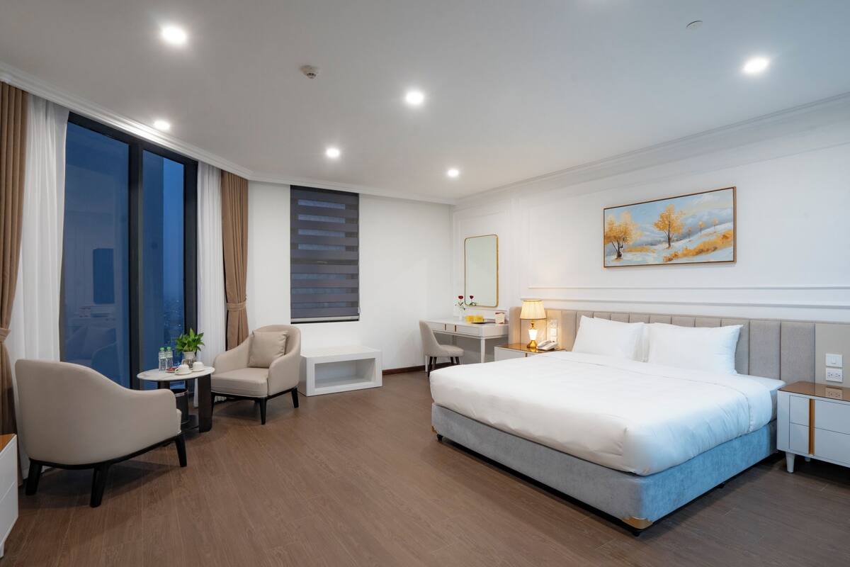 A hotel room with a bed, desk, chair, and a large window.
