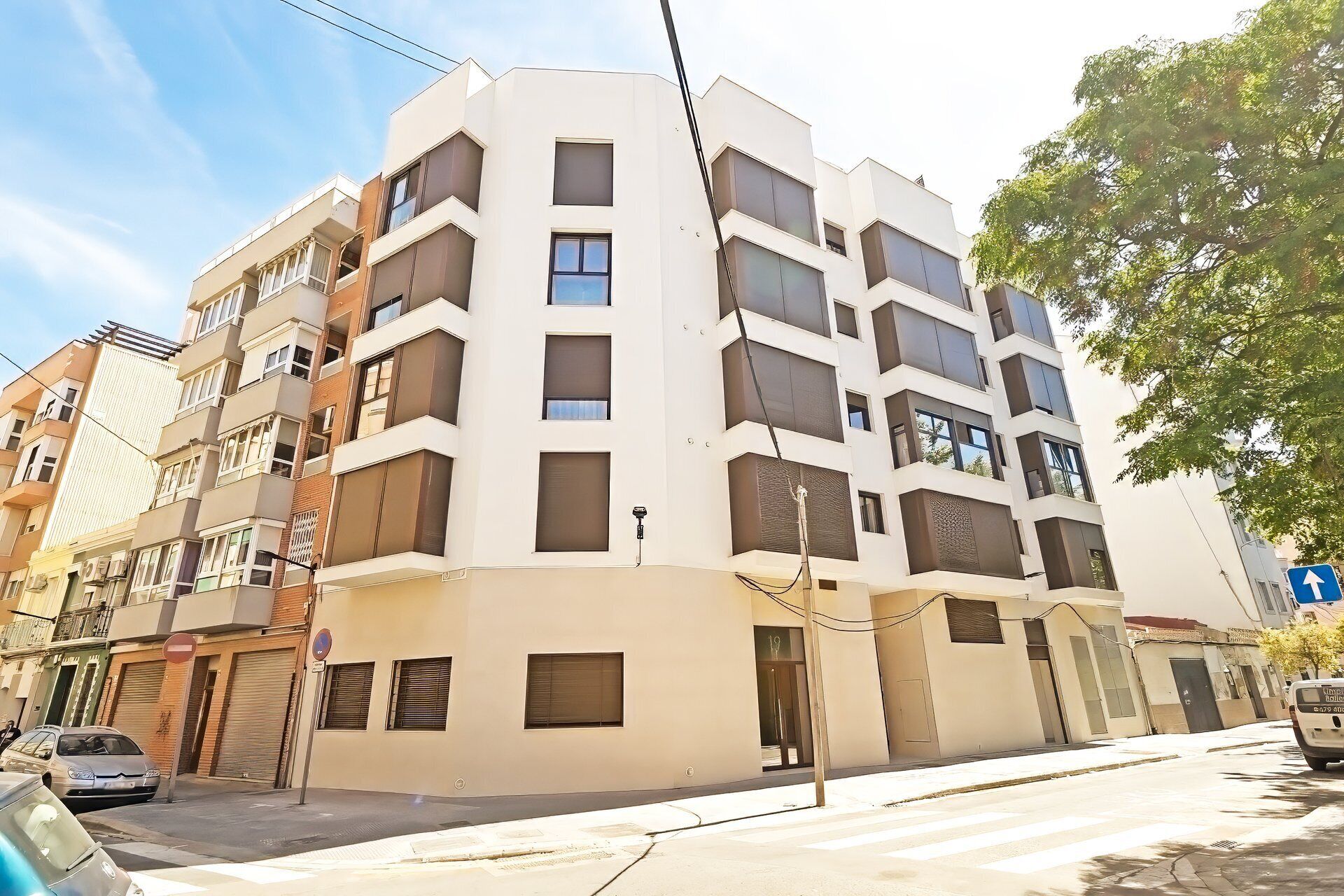 A multi-story residential building with balconies, a gated entrance, and a clear sky.