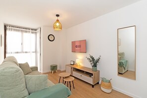 A modern living room with a sofa, a small table, a TV, a clock, a mirror, and a wall-mounted sign. - GuestReady - Modern flat 5 minutes from the beach (Valencia)