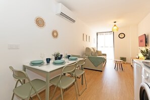 A dining area with a table set for four, a sofa, a washing machine, and a clock on the wall. - GuestReady - Modern flat 5 minutes from the beach (Valencia)