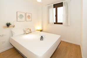 A bedroom with a bed, a nightstand, a window with curtains, a wall-mounted shelf with a plant, and two framed pictures. - GuestReady - Modern flat 5 minutes from the beach (Valencia)