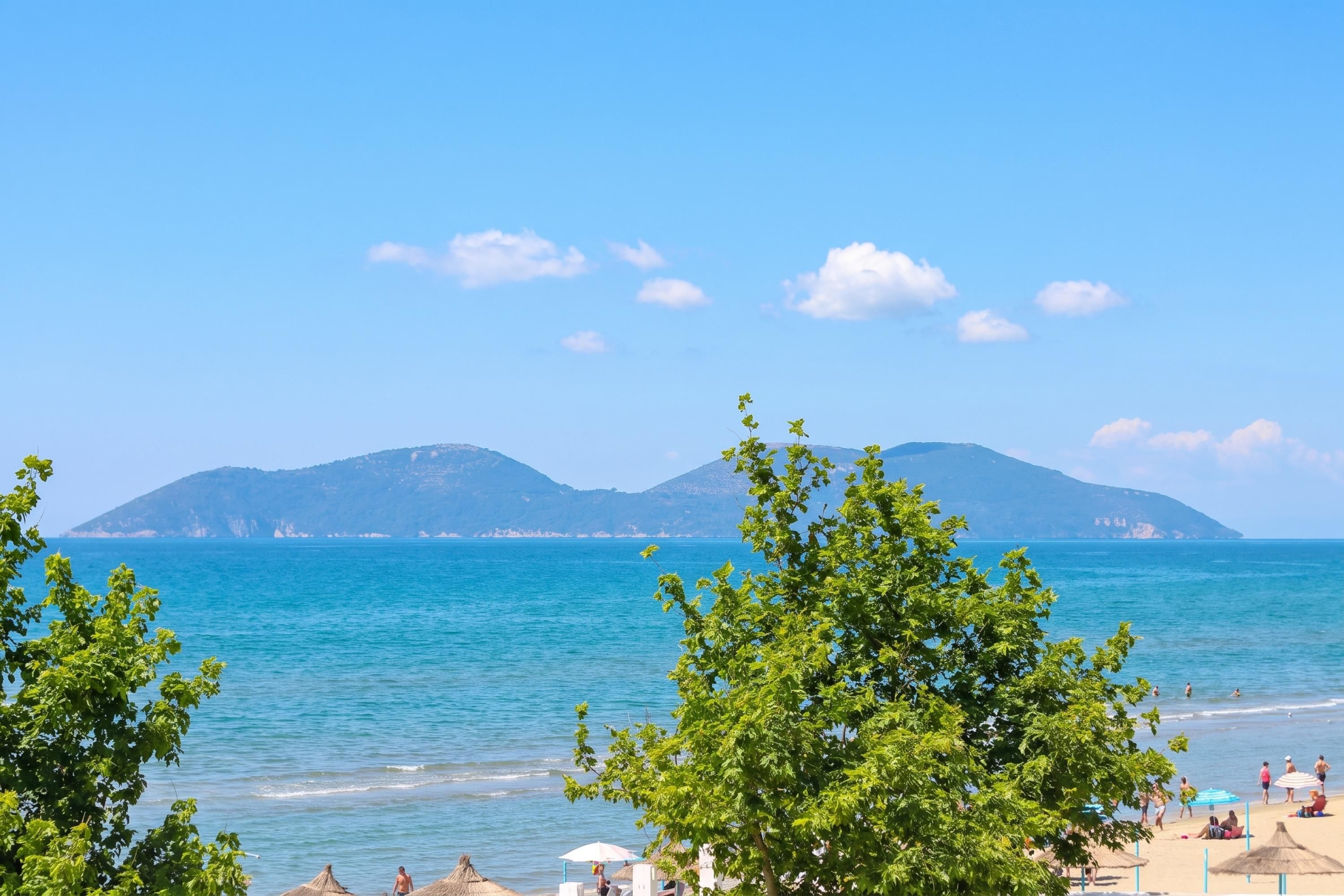A beach with clear blue water, mountains in the background, and people enjoying the beach.