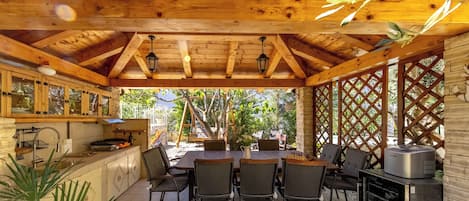 A wooden ceiling with exposed beams, a kitchen with cabinets and a sink, a dining area with a table and chairs, and a refrigerator.