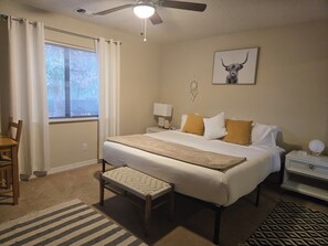 Ein Schlafzimmer mit Bett, Nachttisch, Lampe, Stuhl und Deckenventilator.