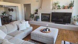 A living room with a sectional sofa, ottoman, fireplace, TV, and various potted plants. - Spacious, zen, fully-equipped 3 bed/2 bath home with red rock views (Sedona)