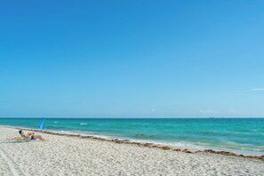 Ein Strand mit einer Person, die auf einem Handtuch liegt, einer blauen Flagge und ruhigem Meer.