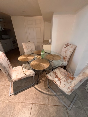 A dining area with a glass table surrounded by four chairs with patterned upholstery, a bottle of water, and a white door in the background.