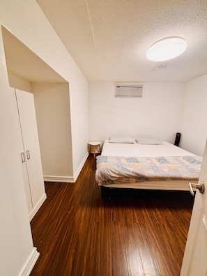 Ein Schlafzimmer mit einem Bett, einem Kleiderschrank, einem kleinen Hocker und einer Deckenleuchte.