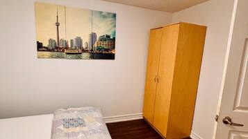 Une chambre à coucher avec un lit, une armoire en bois, un tableau représentant un paysage urbain et une porte.